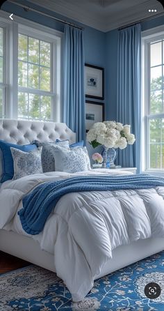 a bedroom with blue walls and white bedding, large windows, and a rug on the floor