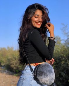 a woman is smiling and holding a furry purse in her hand while standing on a dirt road