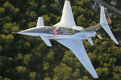 an aerial view of a white fighter jet flying through the air with trees in the background