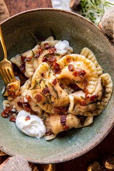 a bowl filled with pasta and bacon on top of a wooden table next to a fork