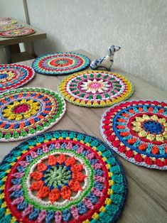 colorful crocheted coasters are arranged on a wooden table with a small bird