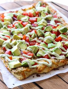 a pizza topped with avocado, tomatoes and cucumber on top of a piece of parchment paper