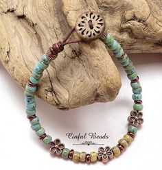 a beaded bracelet with flowers and beads on a piece of wood next to a rock