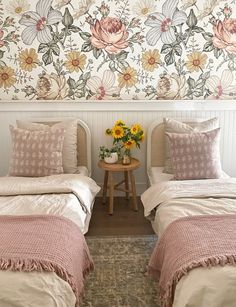 two twin beds in a room with floral wallpaper on the walls and side tables