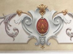 an ornate painting on the wall with gold and red accents, including swirls and scrolls