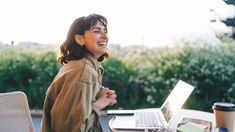 a woman sitting at a table with a laptop computer on her lap and looking up to the sky