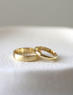 two gold wedding rings sitting on top of a white surface