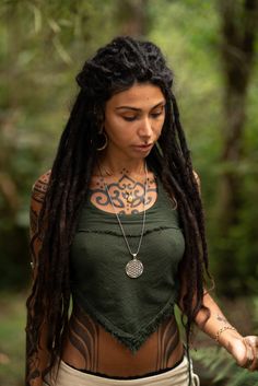 a woman with long dreadlocks and tattoos on her chest standing in the woods