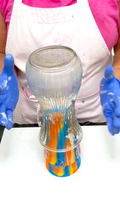 a woman in an apron and blue gloves is making something out of colored liquid with her hands