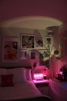 a bedroom with pink lighting and pictures on the wall above the bed in front of it