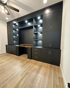 an empty room with wooden floors and black cabinets in the center is a ceiling fan