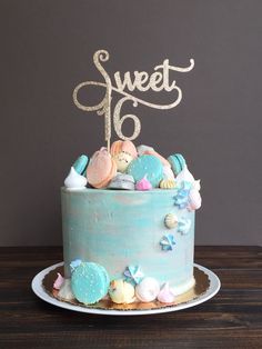 there is a blue cake with shells on it and the word sweet sixteen written in gold
