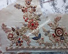 an embroidered piece with red, white and blue flowers on it sitting on top of a bed