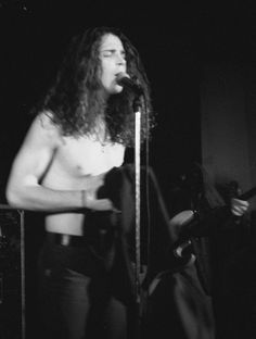 a man with long hair standing in front of a microphone