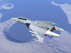 a fighter jet flying through the sky over land and water with clouds in the background