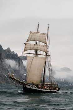 an old sailing ship in the ocean with mountains in the background