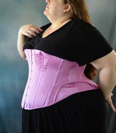 a woman wearing a pink corset and black dress with her hands on her hips