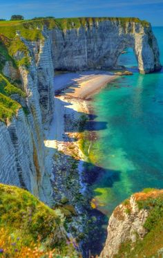 the cliffs and blue water at the beach are covered in green grass, with white cliffs on either side