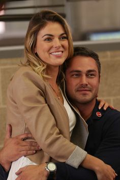 a man and woman hugging each other in front of a brick wall with a clock on it