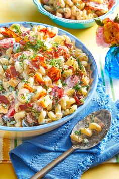 two bowls filled with pasta salad on top of a yellow table cloth next to flowers