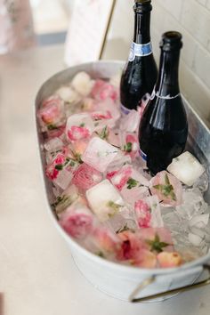 two bottles of beer are sitting in an ice bucket filled with pink and white flowers
