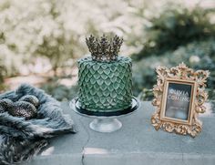 a green cake sitting on top of a table next to a framed photo and pine cones