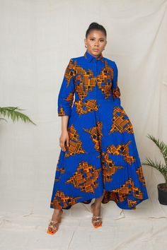 a woman standing in front of a white backdrop wearing a blue dress with orange and yellow designs