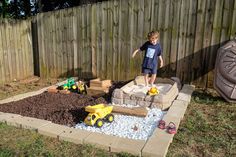 a young boy standing in the middle of a yard with toys and gravel around him