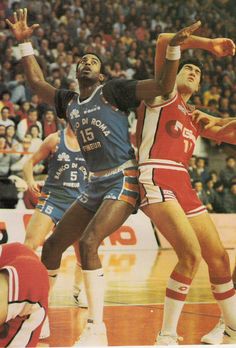 two men are playing basketball in front of an audience at a sporting event, one is reaching for the ball