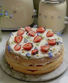 a cake with white frosting and strawberries is on a plate next to two toasters