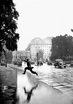 a man jumping in the air on a rainy street with cars and buildings behind him