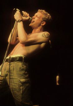 a man with tattoos on his arm holding a microphone and singing into the microphone in front of him