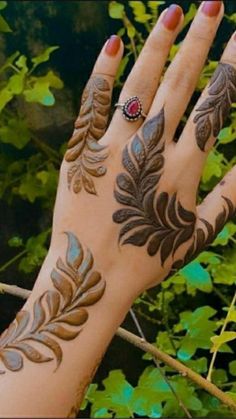 a woman's hand with tattoos on it and green leaves around her wrist, in front of some trees