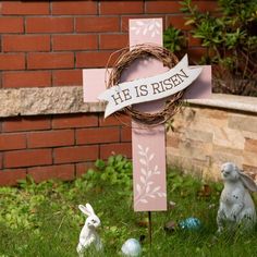 a cross with a wreath on it next to easter eggs and bunny statues in the grass