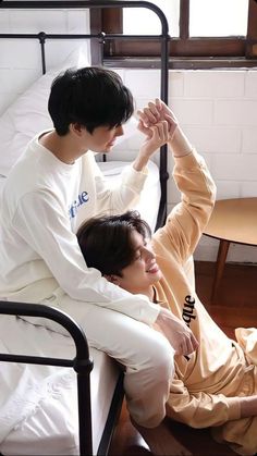 two young men sitting on top of a bed next to each other in white pajamas