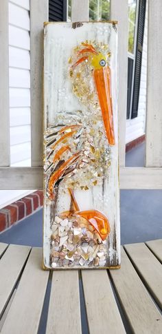 an orange and white bird made out of sea shells on a wooden table next to a house