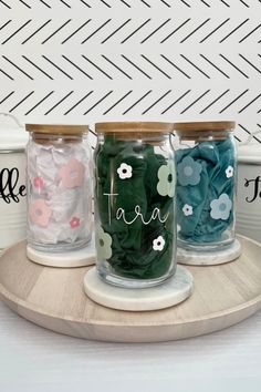 three glass jars with flowers and the words teal on them are sitting on a wooden tray