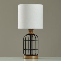 a table lamp with a white shade on it and a black cage around the base