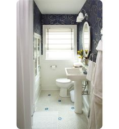 a white toilet sitting next to a bathroom sink under a window in a blue and white bathroom