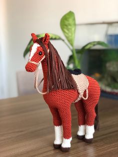 a crocheted toy horse sitting on top of a wooden table next to a potted plant