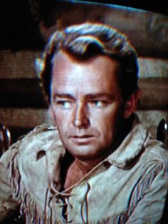 a man is looking at the camera while wearing a cowboy hat and jacket in front of a television screen