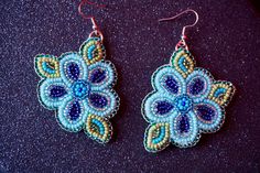 two pairs of blue and green beaded earrings on a black surface, with red thread