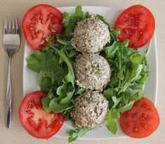 a white plate topped with meatballs covered in lettuce and tomatoes next to a fork