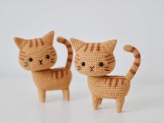 two crocheted cats standing next to each other on a white surface with one cat looking at the camera