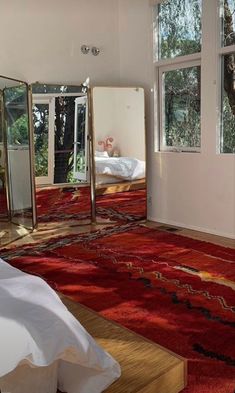 a bedroom with a red rug, mirror and bed in the corner next to it