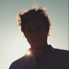 a man standing in front of the sun with his hair blowing in the wind and looking at the camera