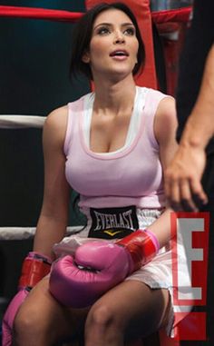 a woman sitting in a boxing ring wearing pink gloves
