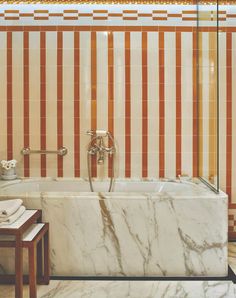 a marble bathtub in a bathroom with orange and white stripes on the wall behind it
