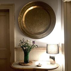a vase filled with flowers sitting on top of a table next to a wall mounted round mirror
