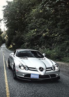 a silver sports car is parked on the side of the road in front of some trees